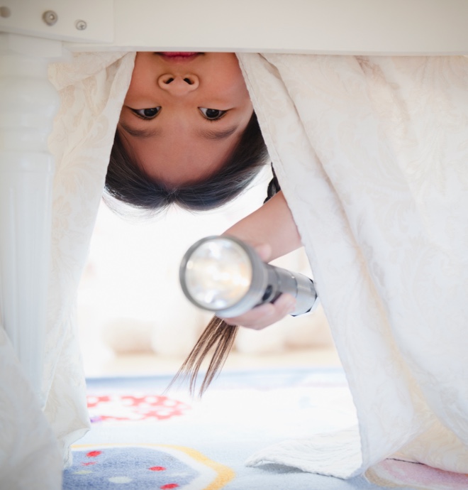 child with flashlight upside down looking under a bed